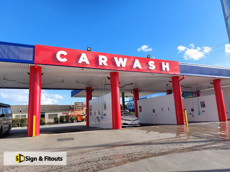 Red CARWASH fascia lettering on a car wash canopy with red columns in Preston