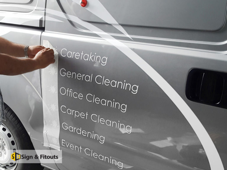 Installer applying white vinyl lettering listing cleaning services to a silver van